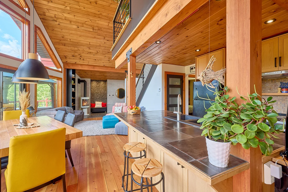 Cuisine et séjour de chalet avec grande fenestration et plafond de bois, par Jonathan Beaupied