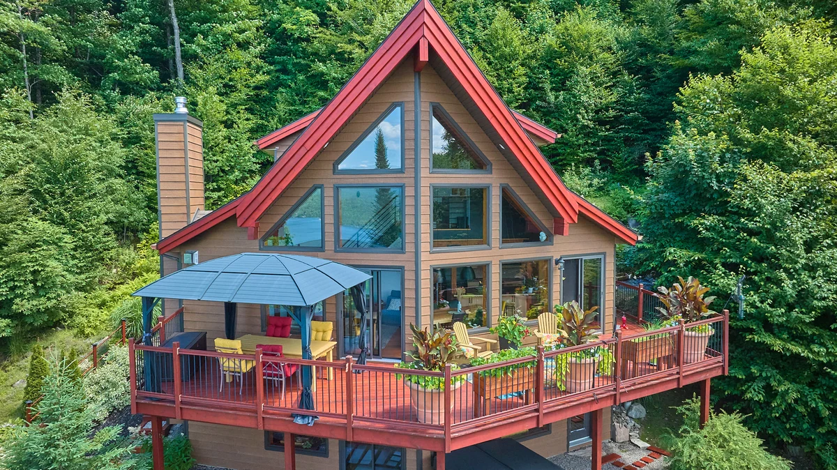 Chalet à toit rouge et terrasse fleurie dans la forêt, vue par drone de Jonathan Beaupied
